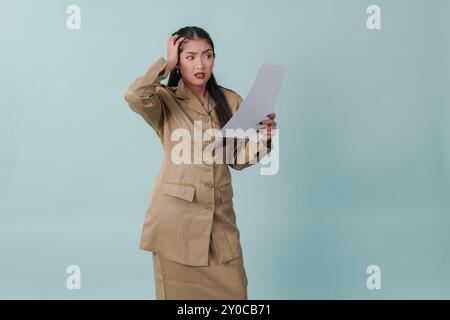 Infastidito lavoratore governativo che indossa l'uniforme cachi che tiene in mano la carta dei documenti con espressione stressante e folle. Concetto di funzionario pubblico PNS. Foto Stock