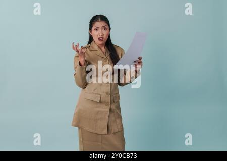 Infastidito lavoratore governativo che indossa l'uniforme cachi che tiene in mano la carta dei documenti con espressione stressante e folle. Concetto di funzionario pubblico PNS. Foto Stock