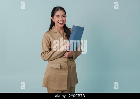 Un giovane e bellissimo lavoratore del governo indonesiano con uniforme cachi che porta documenti e sorrisi alla telecamera. PNS e concetto di funzionario pubblico. Foto Stock
