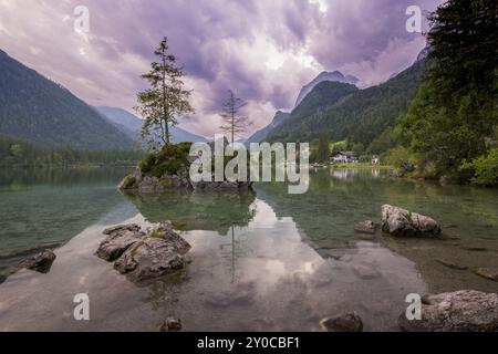 Hintersee con rocce e alberi in primo piano, circondato da montagne dopo il tramonto con un cielo nuvoloso, Ramsau, il Parco Nazionale di Berchtesgaden, Foto Stock