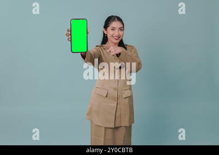 Gioiosa lavoratrice governativa indonesiana che indossa l'uniforme cachi e presenta uno spazio di copia sul suo telefono. Concetto di funzionario pubblico PNS. Foto Stock