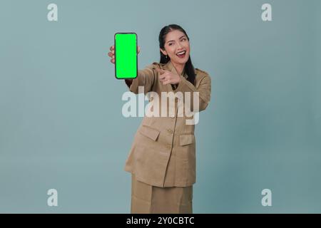 Gioiosa lavoratrice governativa indonesiana che indossa l'uniforme cachi e presenta uno spazio di copia sul suo telefono. Concetto di funzionario pubblico PNS. Foto Stock