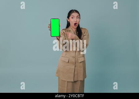 Scioccata lavoratrice governativa indonesiana che indossa l'uniforme kaki presentando uno spazio di copia sul suo telefono. Concetto di funzionario pubblico PNS. Foto Stock