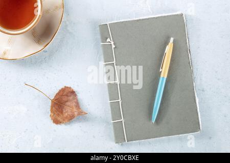 Un diario. Un diario di carta con una penna, una foglia autunnale e una tazza di tè, foto a soffitto su una scrivania, fotografia gastronomica Foto Stock