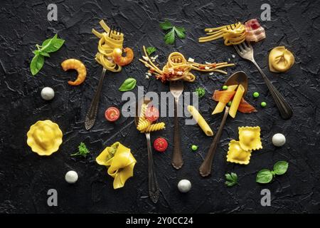 Forchette per pasta varie. Spaghetti, fusilli, penne e altre forme di pasta, con sugo, posa piatta sopra la testa su sfondo nero ardesia. Bolognese, C. Foto Stock