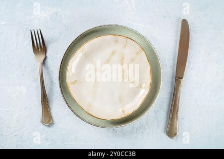 Un piatto vuoto con bordo dorato, argenteria, colpo di posa piatto sospeso. Stoviglie moderne, fotografia gastronomica Foto Stock