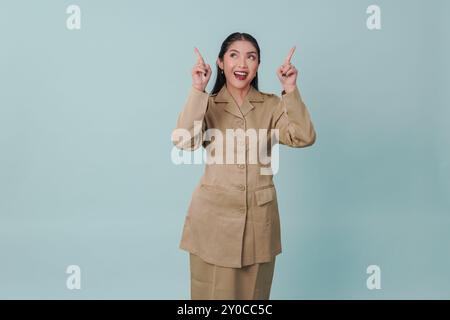 Allegra lavoratrice del governo indonesiano che indossa l'uniforme cachi che indica lo spazio di copia verso l'alto. Concetto di funzionario pubblico PNS. Foto Stock