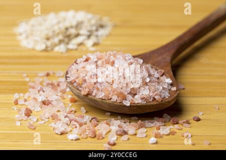 Una foto ravvicinata dello studio di sale rosa grossolano dell'himalaya su un cucchiaio di legno e una pila di avena secca sullo sfondo Foto Stock