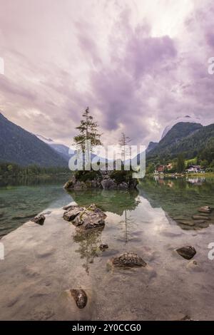 Hintersee con rocce e alberi in primo piano, circondato da montagne dopo il tramonto con un cielo nuvoloso, Ramsau, il Parco Nazionale di Berchtesgaden, Foto Stock