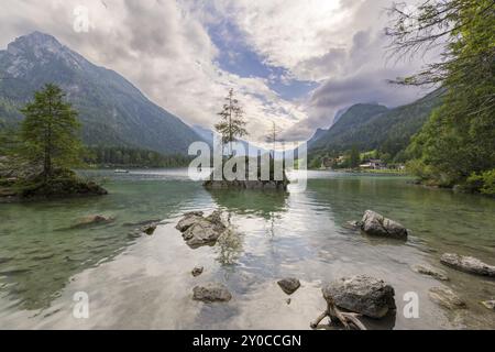 Hintersee con rocce e alberi in primo piano, circondato da montagne dopo il tramonto con un cielo nuvoloso, Ramsau, il Parco Nazionale di Berchtesgaden, Foto Stock