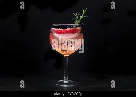 Cocktail elegante con frutta fresca. Gin e bevanda tonica con ghiaccio a una festa, su sfondo nero. Alcol con pompelmo rosa e rosmarino, foto cibo Foto Stock