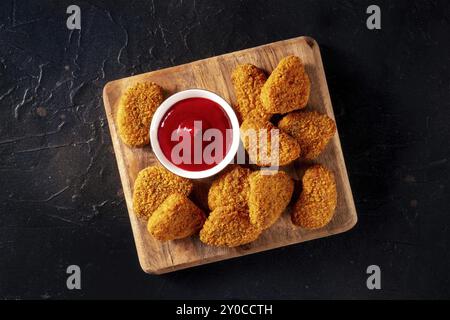 Pepite di pollo con ketchup su sfondo nero, colpo di posa piatto. Uno spuntino croccante a base di carne in un ristorante, un piatto fast food, fotografia gastronomica Foto Stock