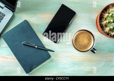 Scrivania, vista dall'alto su sfondo blu di legno. Caffè, notebook, telefono, impianto e laptop, colpo di posa piatto sospeso. Layout di lavoro, Fotografia alimentare Foto Stock