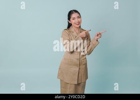 Felice lavoratrice del governo indonesiano che indossa l'uniforme kaki che indica lo spazio di copia accanto a lei. Concetto di funzionario pubblico PNS. Foto Stock
