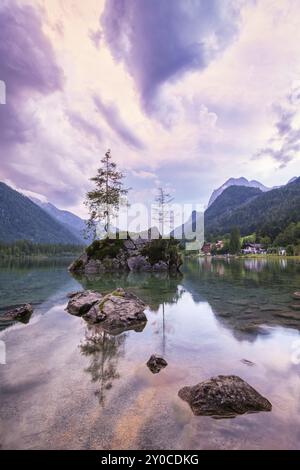 Hintersee con rocce e alberi in primo piano, circondato da montagne dopo il tramonto con un cielo nuvoloso, Ramsau, il Parco Nazionale di Berchtesgaden, Foto Stock