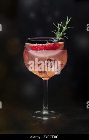 Cocktail elegante con frutta fresca. Gin e bevanda tonica con ghiaccio a una festa, su sfondo nero. Alcool con pompelmo rosa e rosmarino, imag tonificato Foto Stock