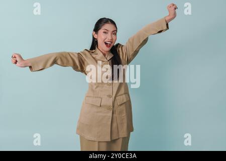 Eccitata donna indonesiana lavoratrice del governo che indossa l'uniforme cachi in posa con una felice espressione di successo. Concetto di funzionario pubblico PNS. Foto Stock