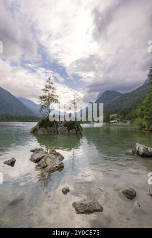 Hintersee con rocce e alberi in primo piano, circondato da montagne dopo il tramonto con un cielo nuvoloso, Ramsau, il Parco Nazionale di Berchtesgaden, Foto Stock