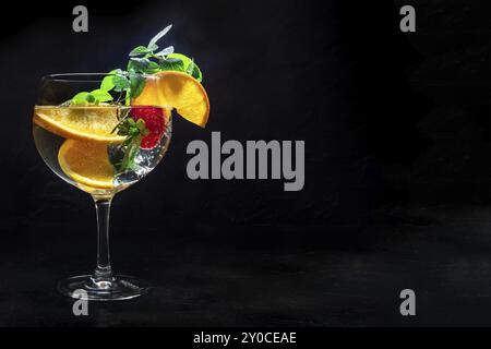 Cocktail elegante con frutta fresca. Gin e bevanda tonica con ghiaccio a una festa, su sfondo nero. Alcol con arancia, menta e fragola, con copia Foto Stock