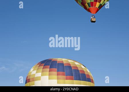 Coloratissima mongolfiera pronto per alzarsi in volo e un altro già in volo contro un cielo blu Foto Stock