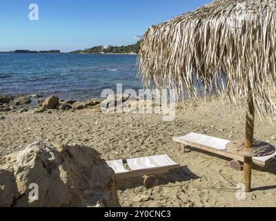 Spiaggia sabbiosa con lettini e tetto in paglia, circondata da rocce e affacciata sul mare con il sole, katakolon, mediterraneo, gre Foto Stock