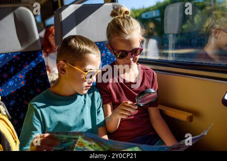 Fratelli seduti in treno, che guardano la mappa con una lente d'ingrandimento. La famiglia fa un'escursione, usando i mezzi pubblici. Foto Stock