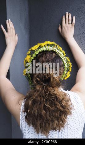 Donna stretching contro un muro grigio con una ghirlanda di fiori in un bellissimo marrone capelli ricci Foto Stock