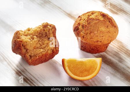 Muffin all'arancia rotti su un tavolo da cucina rustico in legno, con una fetta di frutta fresca Foto Stock