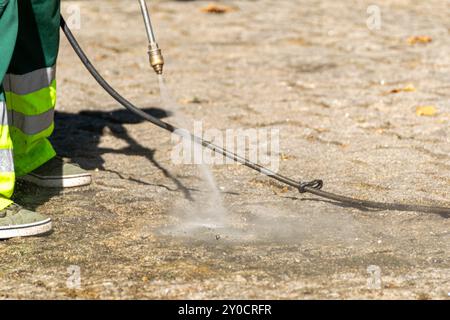 attenzione selettiva, un addetto alle pulizie pubblico che pulisce la strada con acqua ad alta pressione Foto Stock