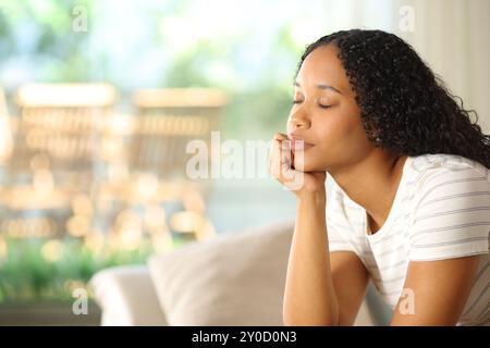 Donna nera che si rilassa a occhi chiusi seduta su un divano a casa Foto Stock