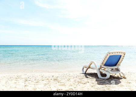 Un lettino da sole bianco e blu si trova sulla riva del mare, proprio accanto all'acqua. Il concetto di una vacanza al mare o all'oceano. Spiaggia privata del Foto Stock