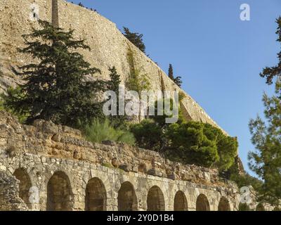 Antico muro di pietra con archi, circondato da alberi e vegetazione sotto un cielo azzurro, atene, grecia Foto Stock