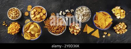 Spuntini salati, mix di festa, panorama piatto sopra la testa. Un assortimento di antipasti. Patata e tortilla patatine, cracker, popcorn ecc banner panoramico Foto Stock