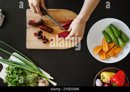 Vista dall'alto delle mani femminili che affettano metà di barbabietola biologica fresca su un tagliere di legno Foto Stock