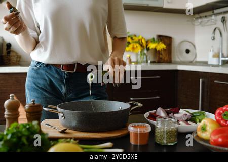 Donna irriconoscibile che versa olio d'oliva in una teglia da forno dalla bottiglia Foto Stock