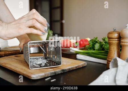 Le mani femminili grattugiano il formaggio di capra utilizzando una grattugia metallica in cucina Foto Stock