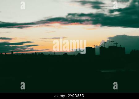 Sagome di edifici alti, gru da costruzione contro un cielo nuvoloso al tramonto. Cantiere. Progetto tecnico. Sviluppo e alloggi. Foto Stock