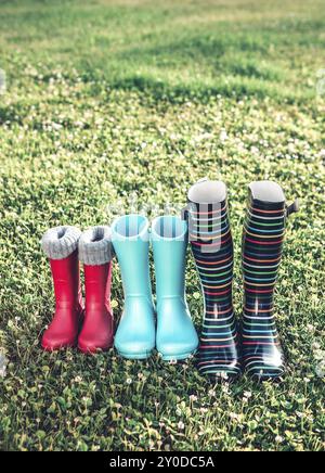 Stivali di gomma rossi e blu a righe per adulti e bambini, disposti su prati con erba verde giovane nelle giornate di sole Foto Stock