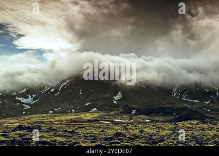 Le nuvole maestose si snodano su una catena montuosa, gettando ombre spettacolari sull'aspro paesaggio sottostante. L'interazione di luce e ombre crea una covata Foto Stock