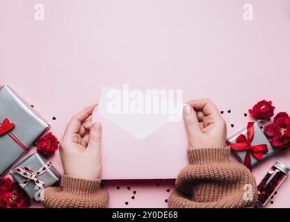 Le mani femminili tengono lettera d'amore vuoto messaggio in busta aperta, biglietto di auguri di San Valentino o invito bianco mock up. Spazio di copia, vista dall'alto. Rosa ba Foto Stock