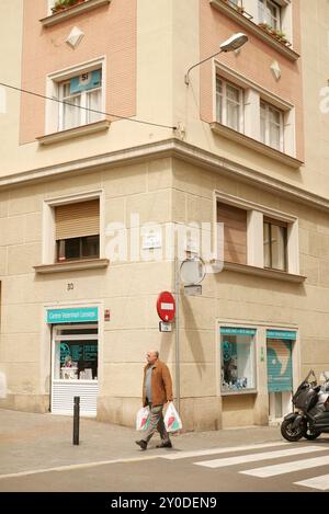 Un uomo che cammina con le borse dello shopping all'angolo tra un edificio architettonico europeo e una passeggiata in moto. Foto Stock