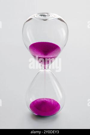Clessidra contenente sabbia rosa isolata su sfondo bianco. Concetto di passaggio del tempo Foto Stock