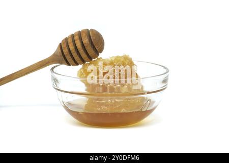 Recipiente di vetro con miele e cucchiaia in legno che poggia sul bordo isolato su fondo bianco, profondità di campo completa Foto Stock