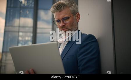 Imprenditore anziano, maturo e concentrato, imprenditore di mezza età, uomo d'affari impegnato, commerciante, vecchio imprenditore in pensione, ha messo gli occhiali che lavorano guardando un notebook Foto Stock