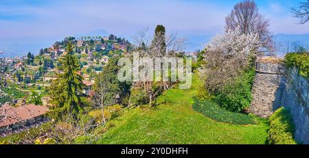 Panorama del bastione medievale in pietra Castello di San Vigilio, fiorito giardino di primavera e Monte Bastia sullo sfondo, Bergamo, Italia Foto Stock