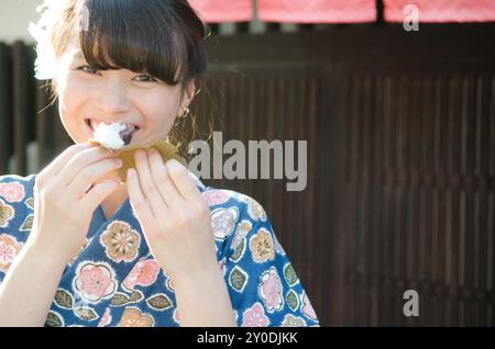 Una donna sorridente che indossa un kimono che mangia torte di riso avvolte in foglie di quercia Foto Stock