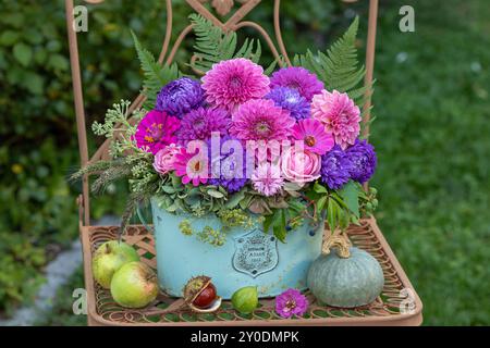 composizione floreale con assaggi estivi viola, dahlia rosa, rose e zinnie in un vaso vintage su una sedia da giardino Foto Stock