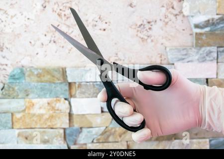 Forbici in mano con guanto in gomma. Cesoie in acciaio per il taglio. Foto Stock