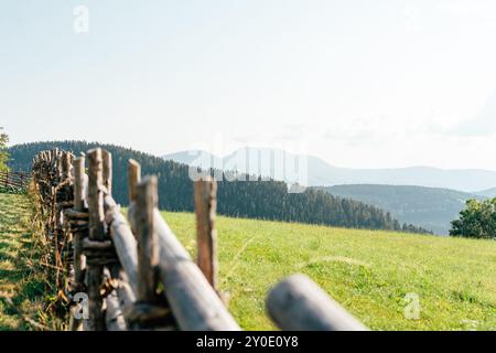 Una recinzione rustica in legno si estende lungo un campo verde con mountai Foto Stock