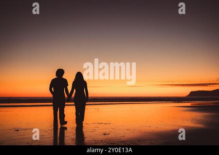 La silhouette di una coppia che cammina sulla spiaggia durante il tramonto Foto Stock